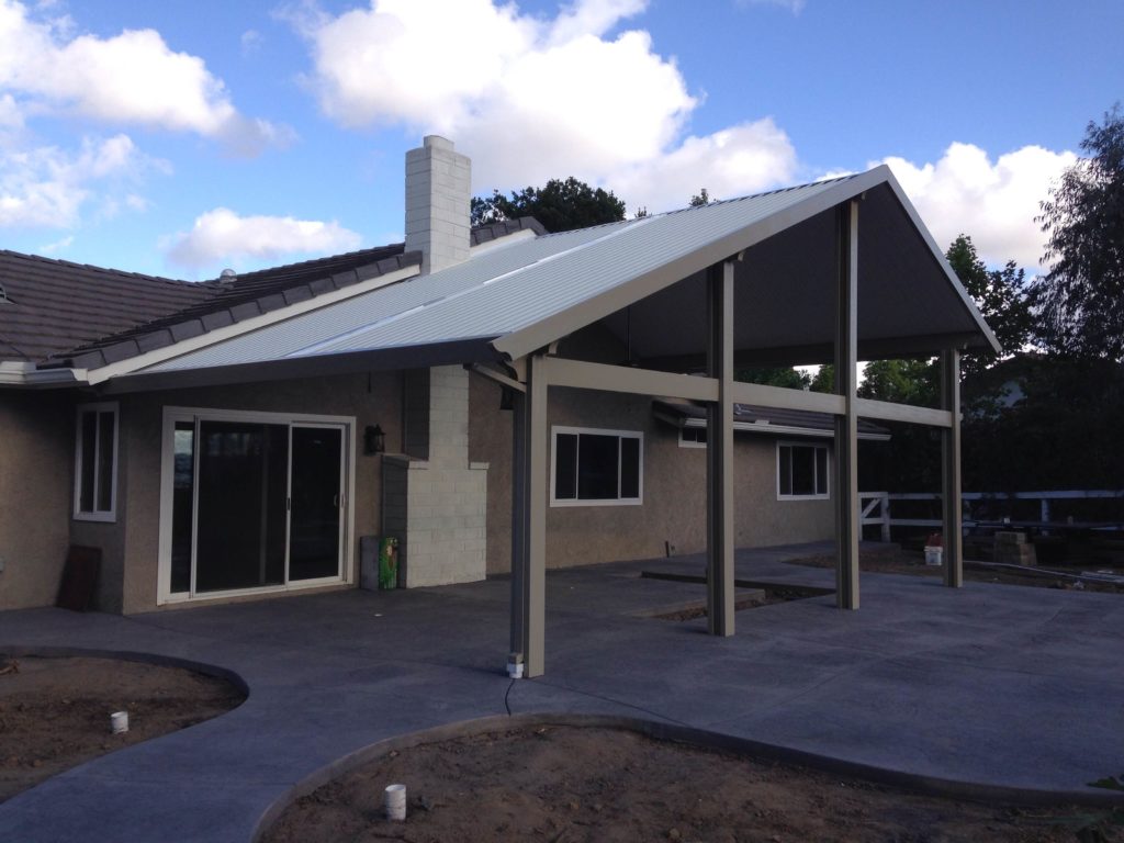 A gable-roofed Newport Solid cover attached to a single-story home over a new concrete patio