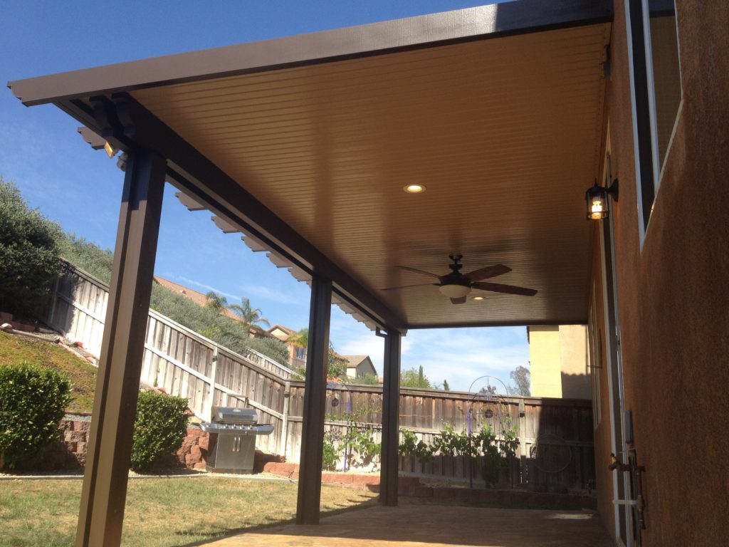 The wood-grain underside of a mocha-brown cover with a dark ceiling fan on a hillside patio