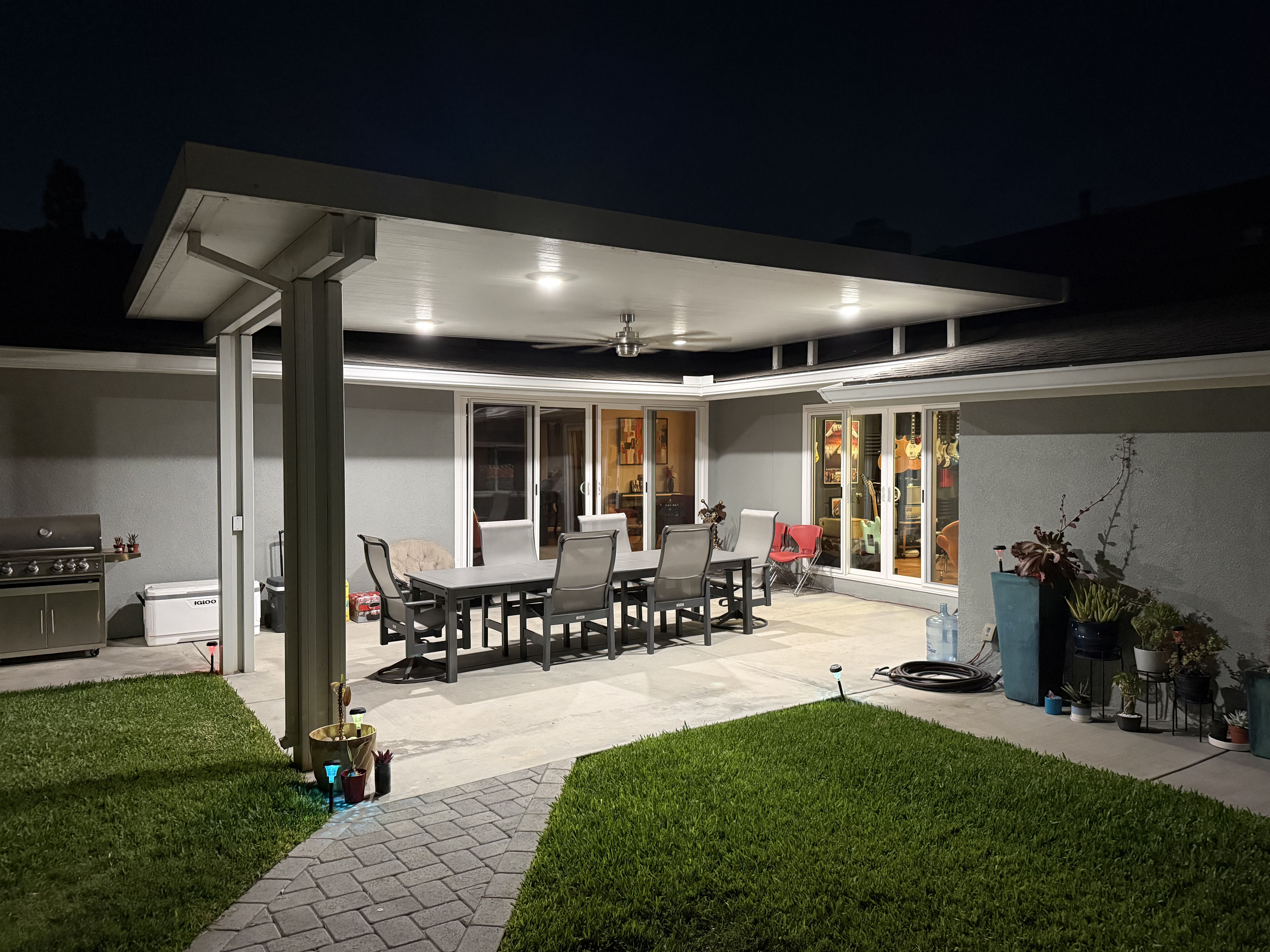 Solid panel patio cover glowing warm at night with recessed lights and ceiling fan over a family dining space